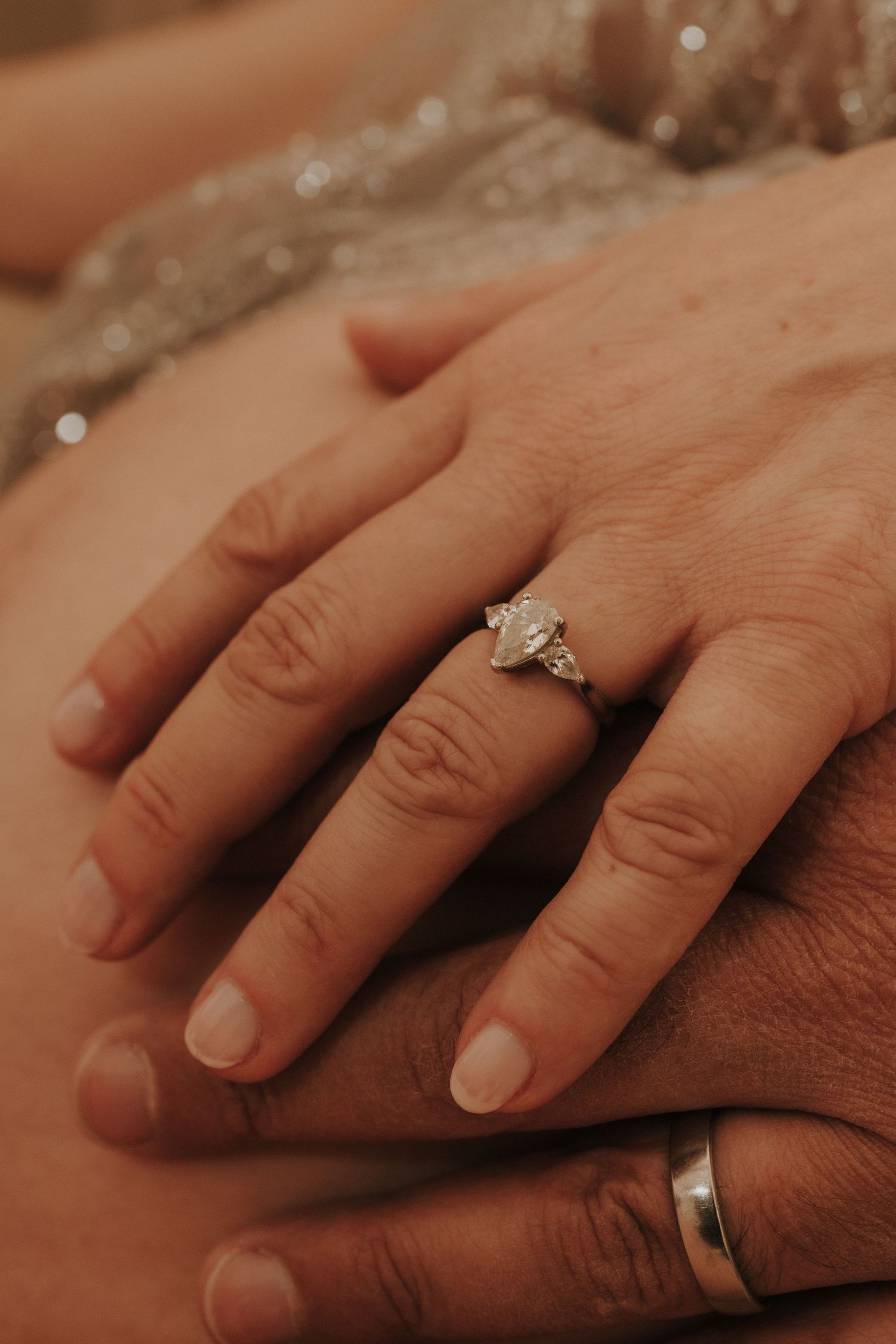 Intimate detail shot of hands with engagement and wedding rings in warm lighting.