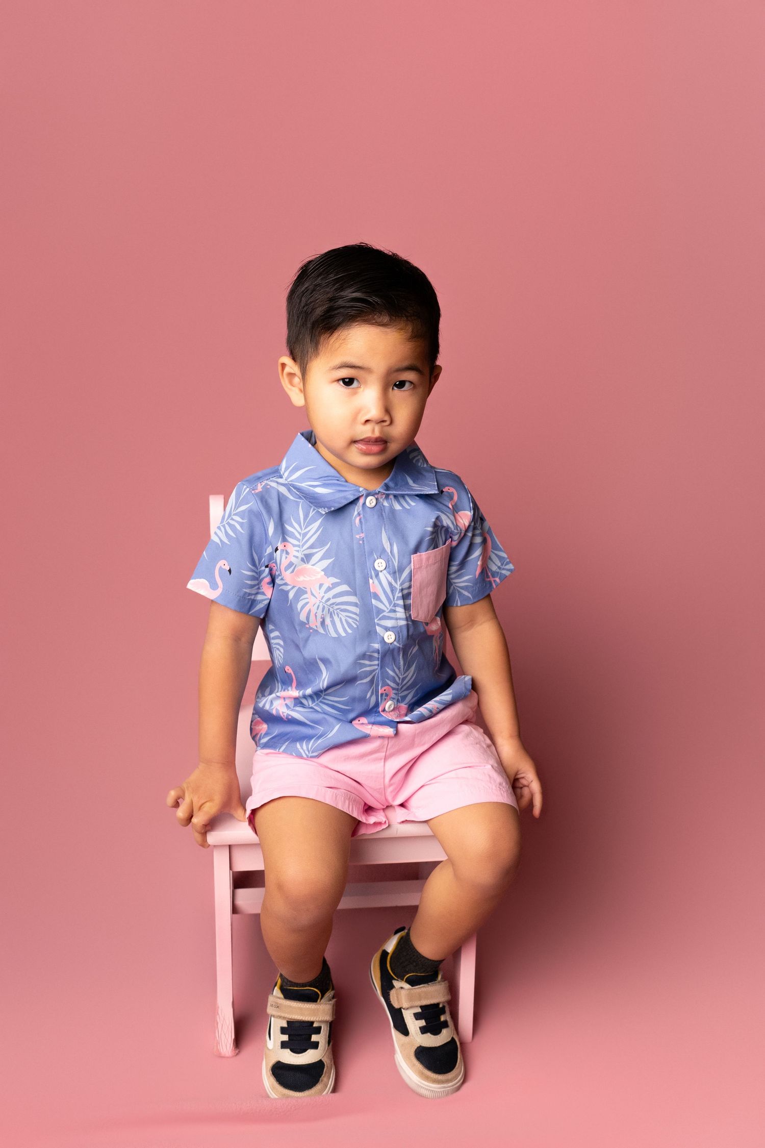 Child sitting in pink chair wearing blue floral outfit with pink shorts.