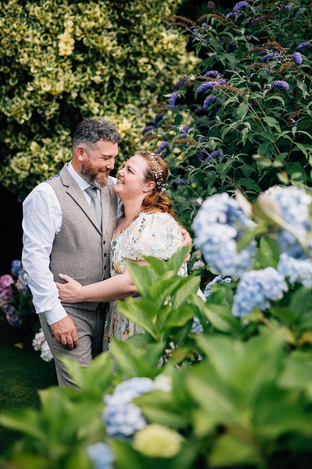 A wedding couple stands by a mountain lake with dramatic peaks in the background.