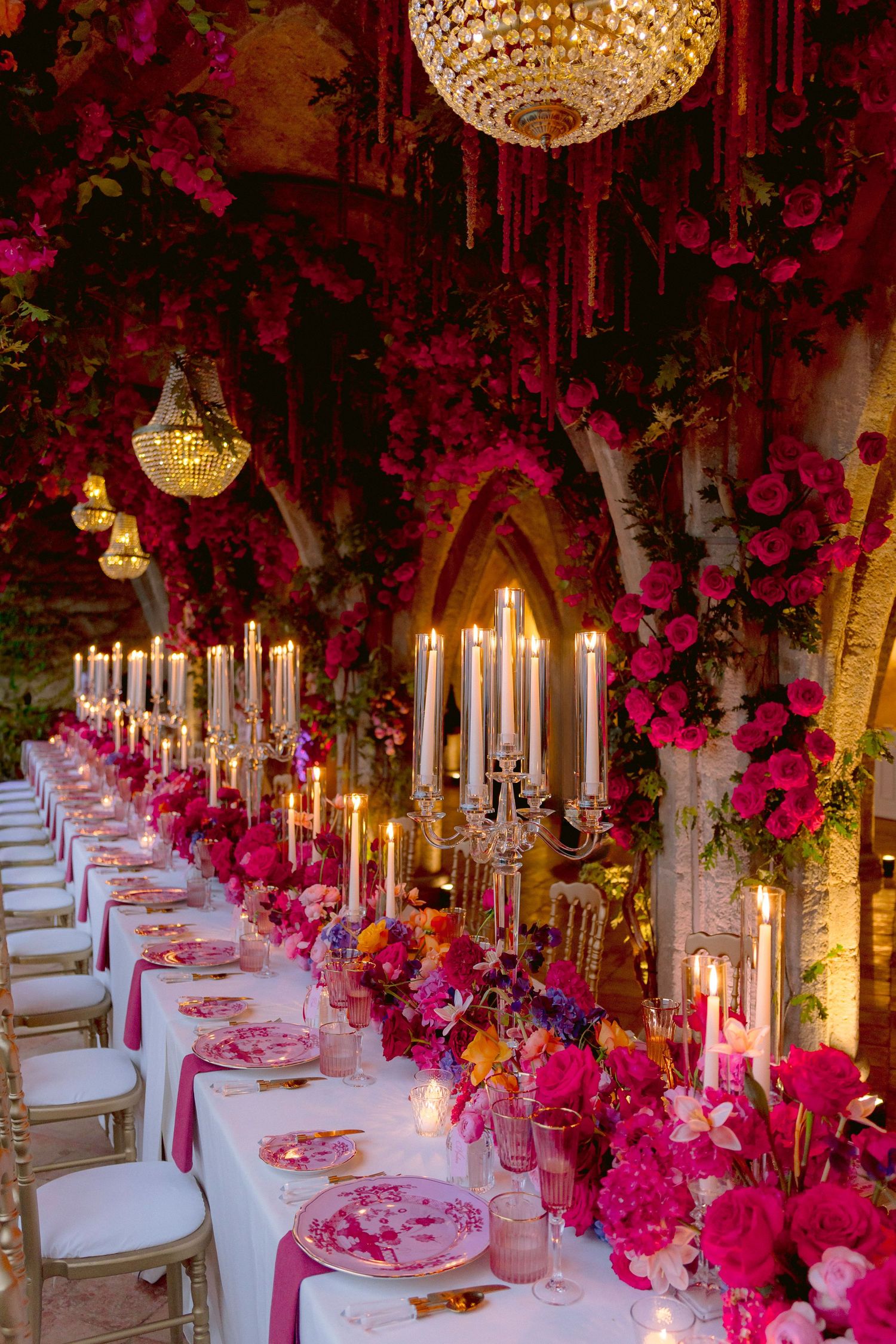 Elegant dinner party setting with crystal chandeliers and pink floral arrangements creating a romantic ambiance.