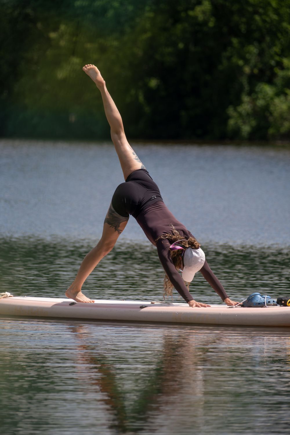 Person practicing yoga on a paddleboard on a calm lake, performing a one-legged downward dog pose outdoors.