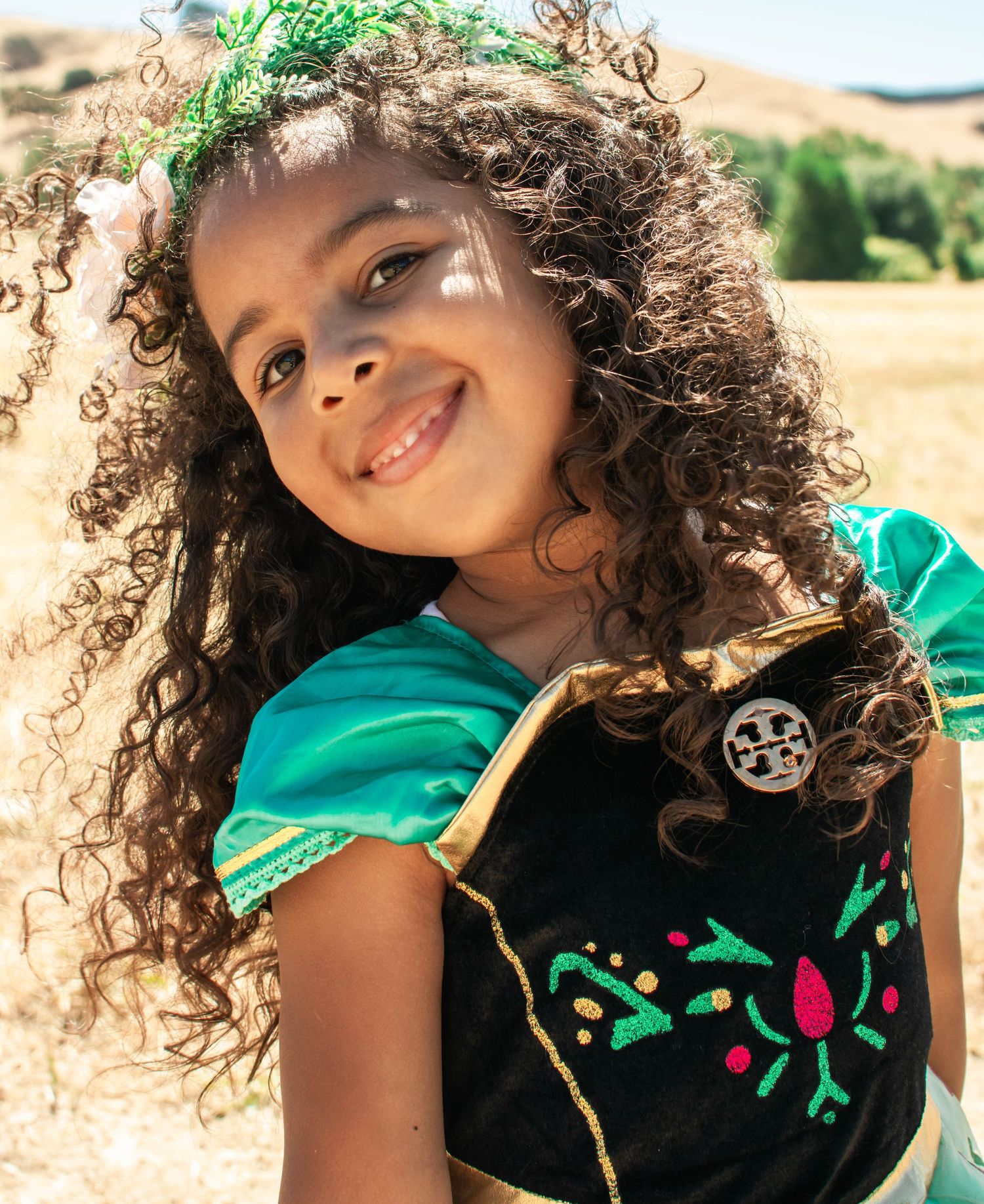 A series of four photos showing a child with curly hair wearing a green and black top in various playful poses outdoors.