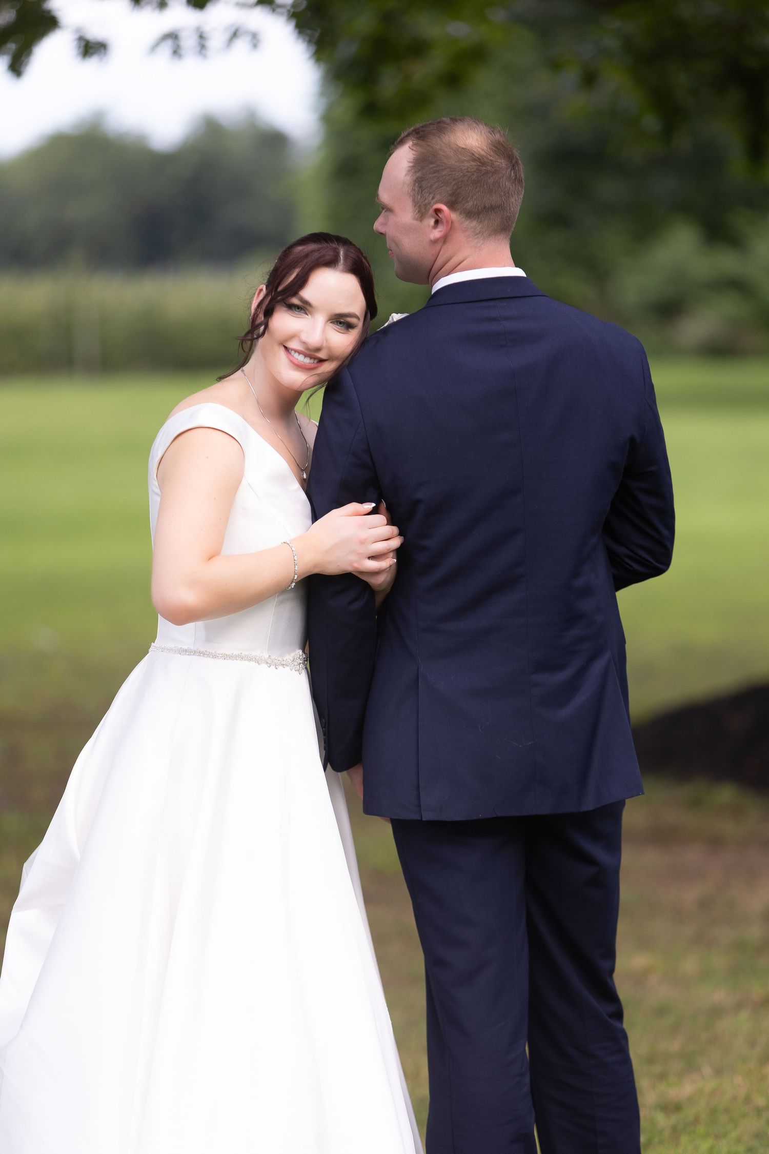 A bride in a white dress and groom in navy suit share an intimate moment outdoors on their wedding day.