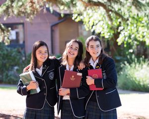 Students in matching uniforms displaying graduation certificates outdoors.