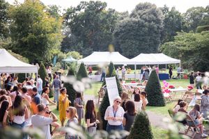 An outdoor summer garden party with white tents and guests mingling on a sunny afternoon.
