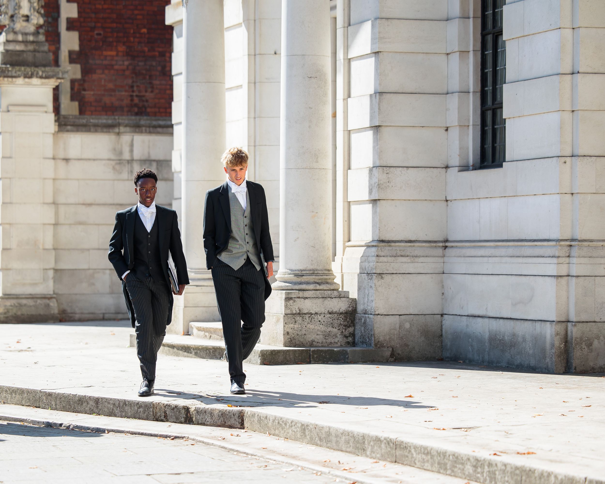 Business professionals walking through a bright marble colonnade hallway with classical architecture.