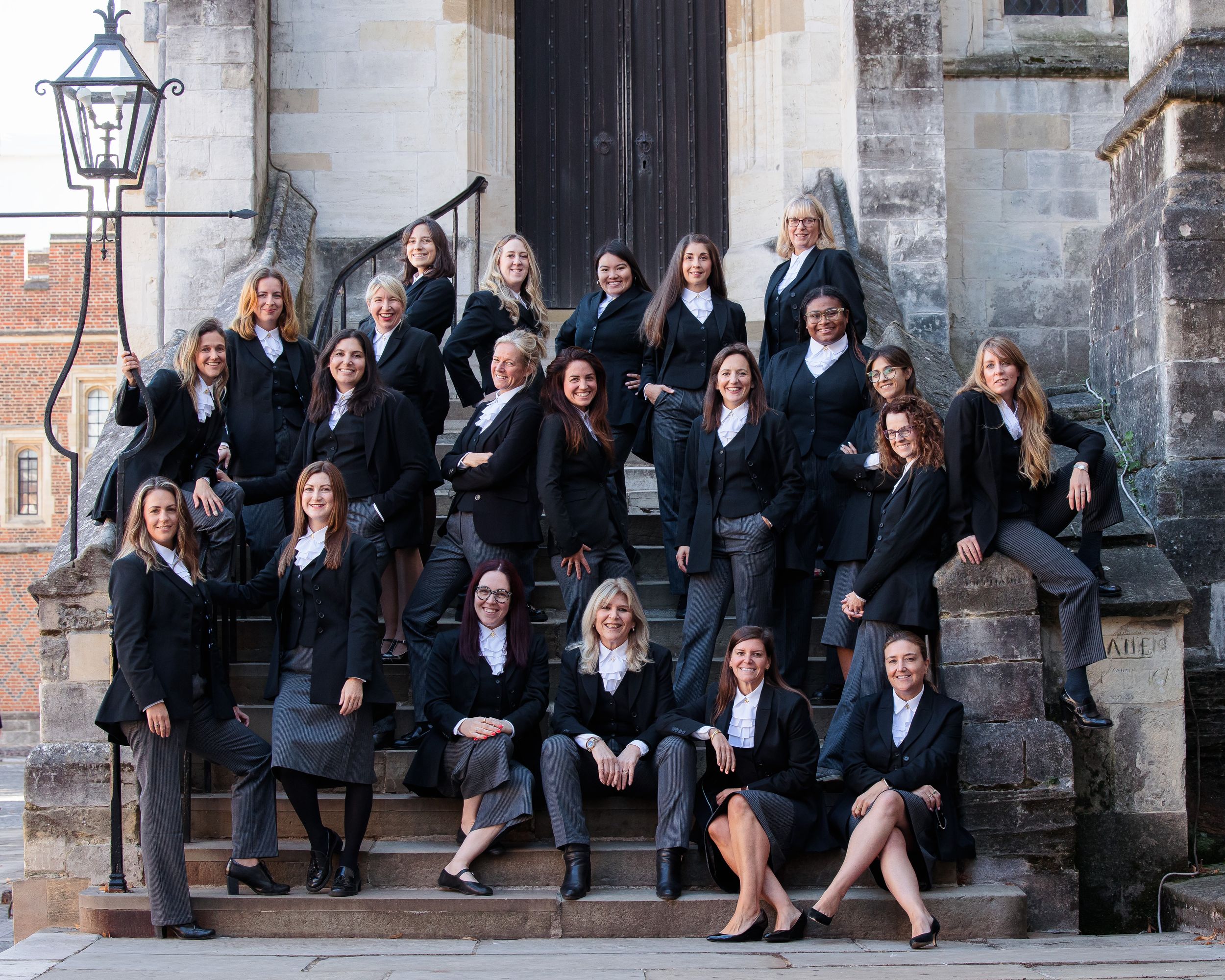 Group photo of graduates in formal attire sitting on stone steps of a historic building.