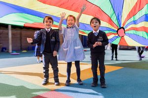 Students play with a colorful parachute on a vibrant playground surface during outdoor activities.