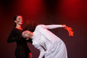Contemporary dancers performing against a dramatic red backdrop on stage.