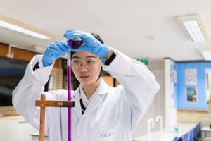 Students in a science lab wearing protective equipment and conducting experiments with test tubes.
