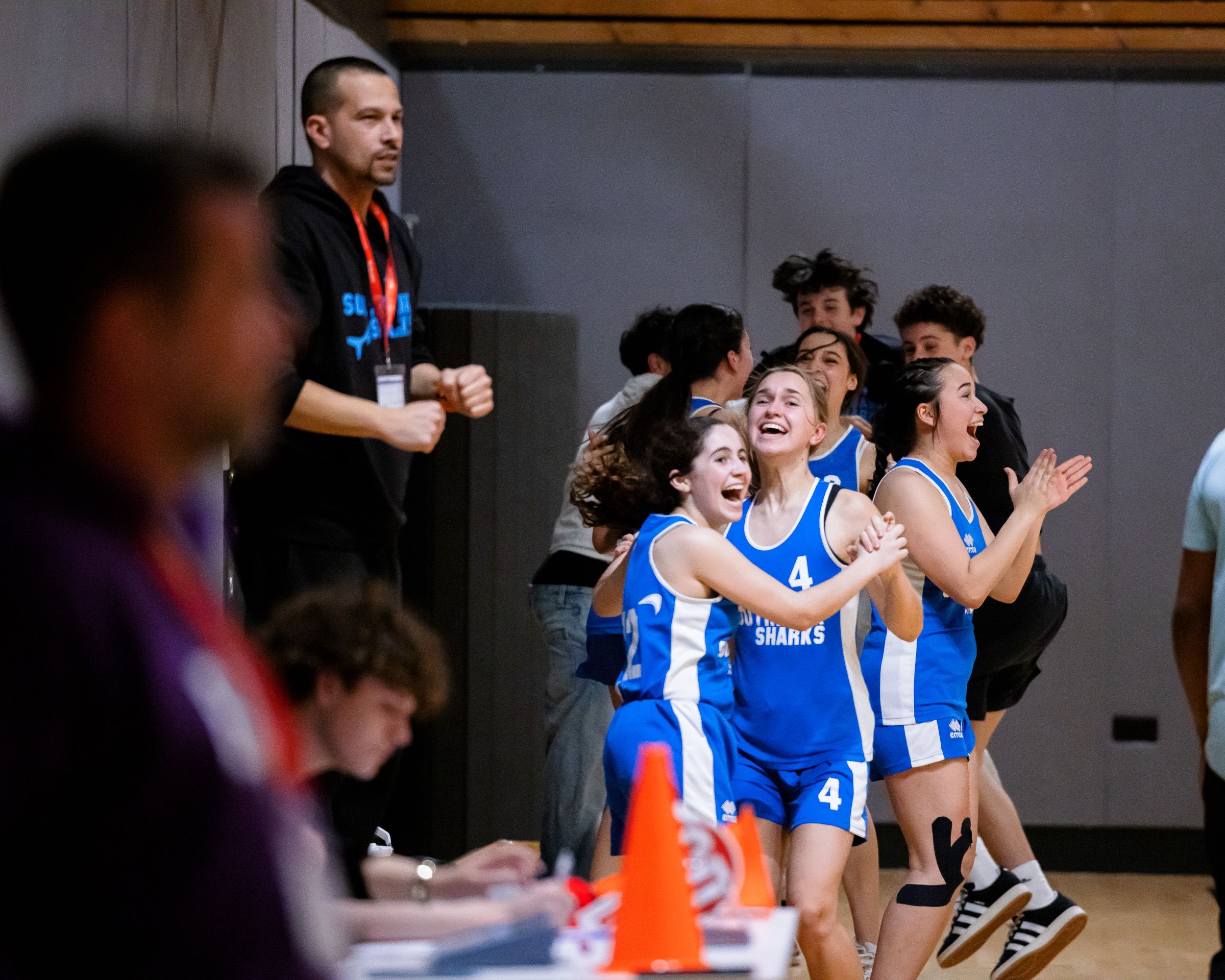 Athletes celebrate during an intense sporting competition with teammates cheering from the sidelines.