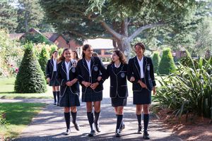 Students walking together on a tree-lined path wearing school uniforms.