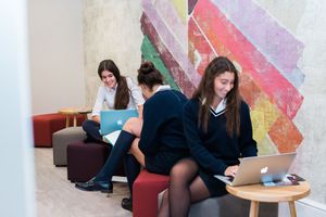 Students in school uniforms study with laptops in a modern lounge area.