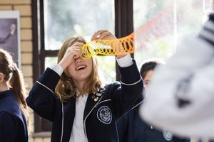 A student in uniform laughs while holding up a trophy in celebration.