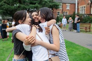Students celebrating and embracing outdoors on a green campus lawn.