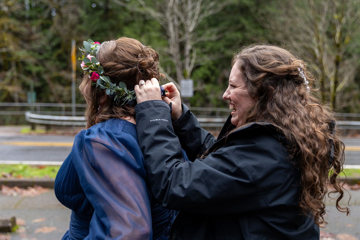 Woman smiling while placing a floral crown on brides hair during outdoor wedding preparation. PNW elopement Photographer.
