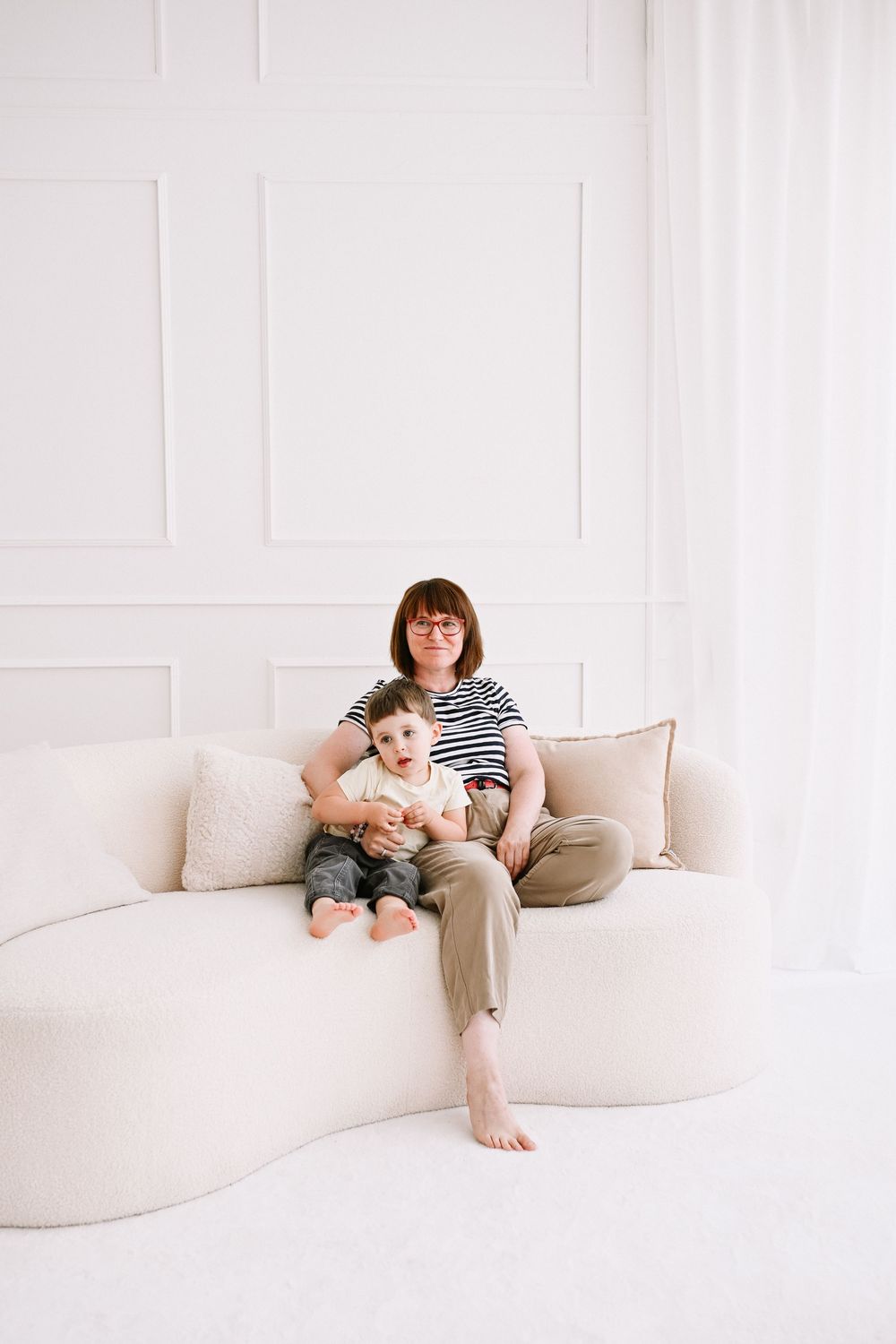 Family lounging together on modern curved sofa in bright white studio setting.