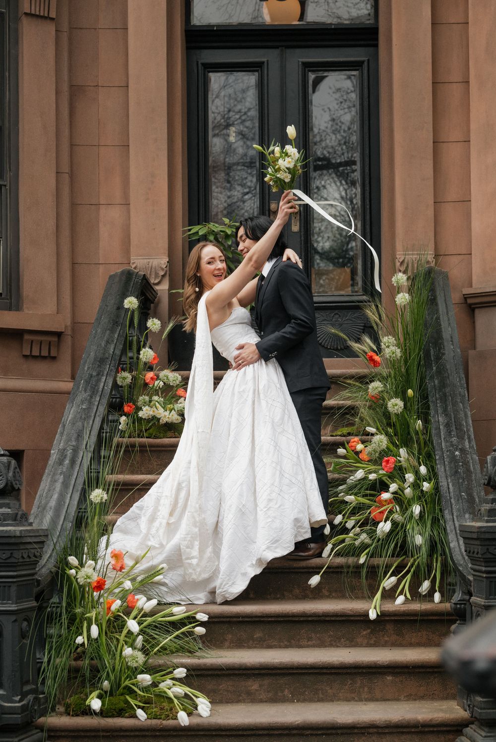 A sequence of wedding photos showing a couple dancing and twirling on brownstone steps decorated with floral arrangements.