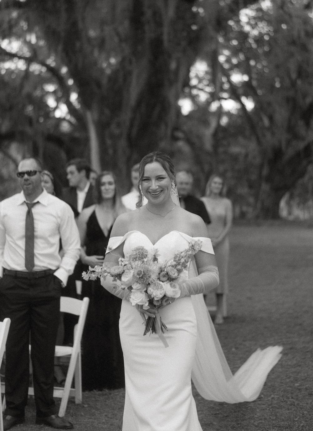 A black and white wedding photo series showing the bride in an off-shoulder white dress holding a bouquet in an outdoor setting.