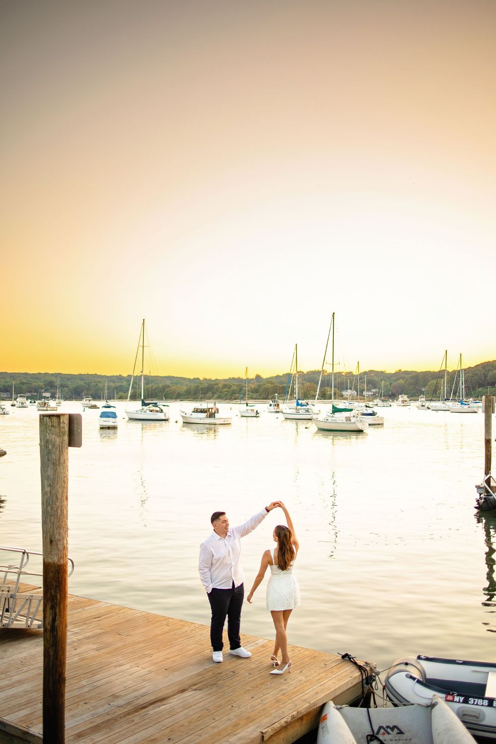 A romantic marriage proposal scene unfolds on a wooden dock at sunset with sailboats in the harbor.