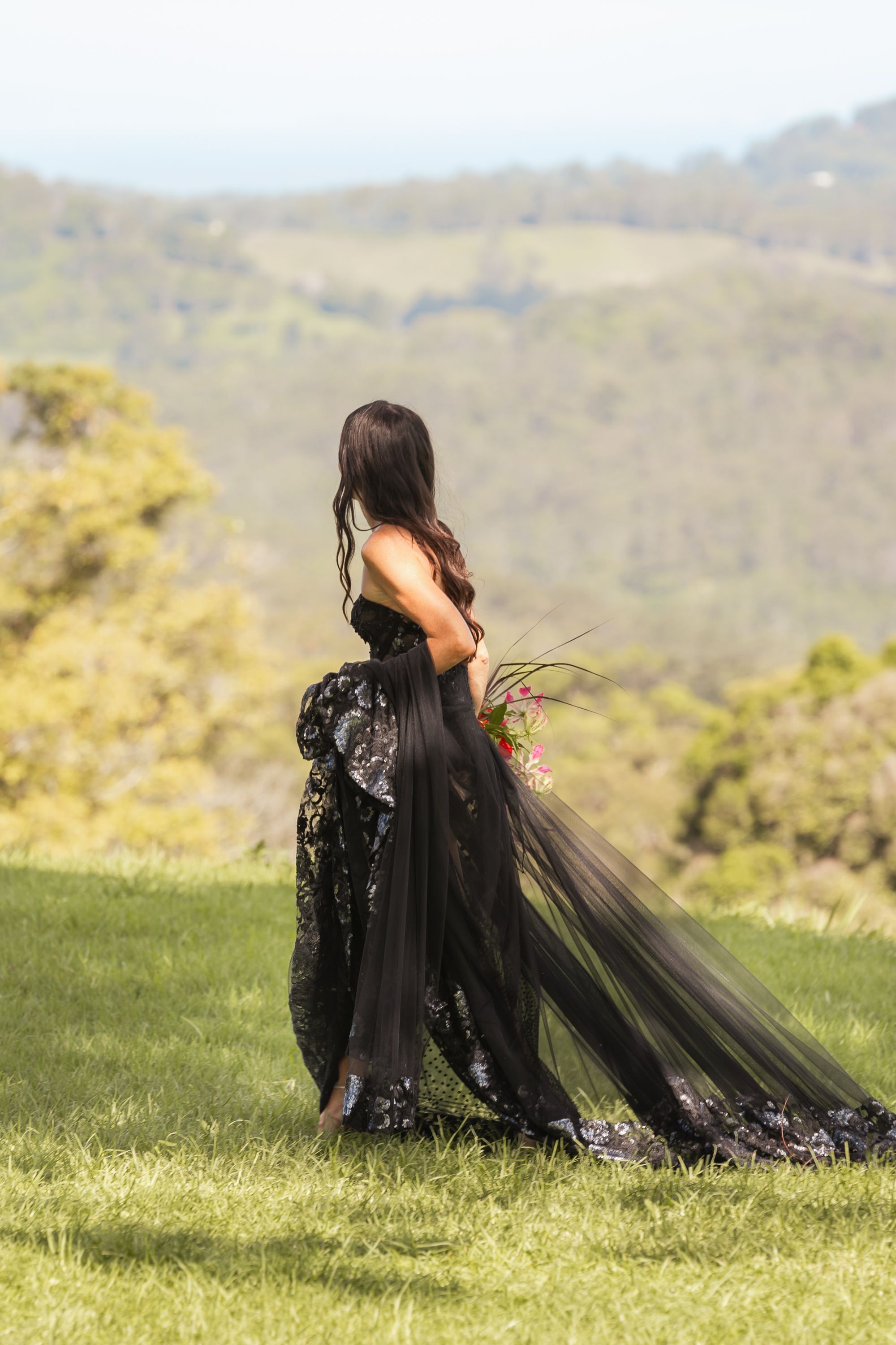 A black tulle dress flows gracefully across green hillside grass during an outdoor photoshoot.