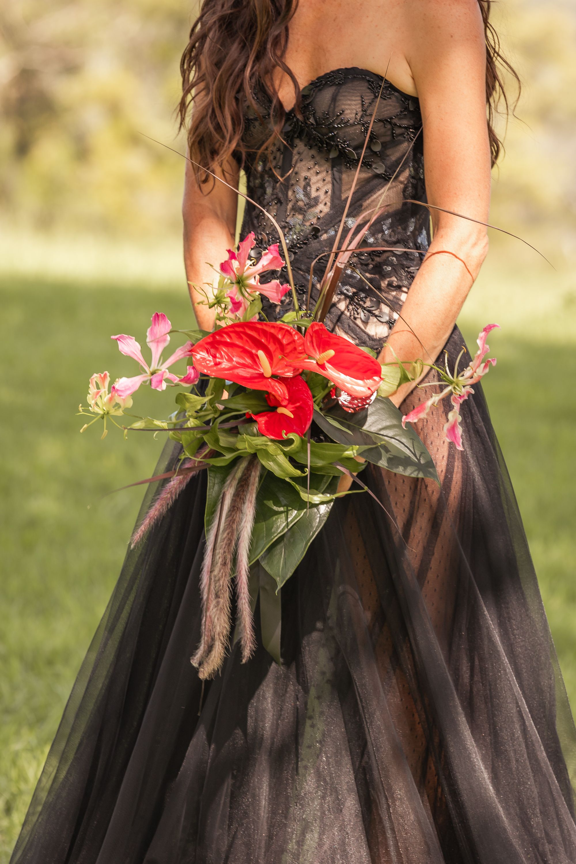 Red flowers accent a dramatic black tulle gown in an outdoor garden setting.
