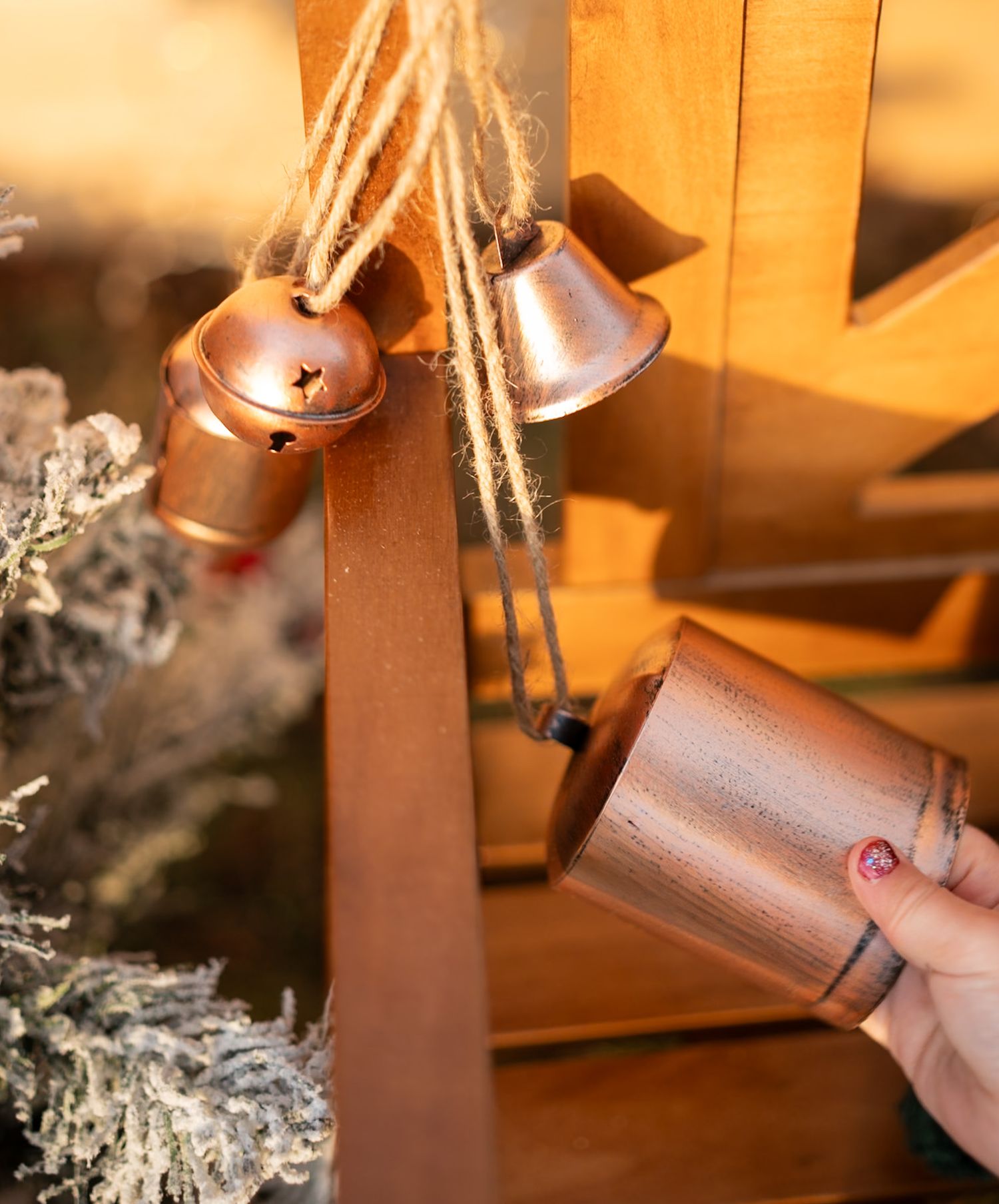 Hand holding copper bell ornament against warm golden background with frosted branches.