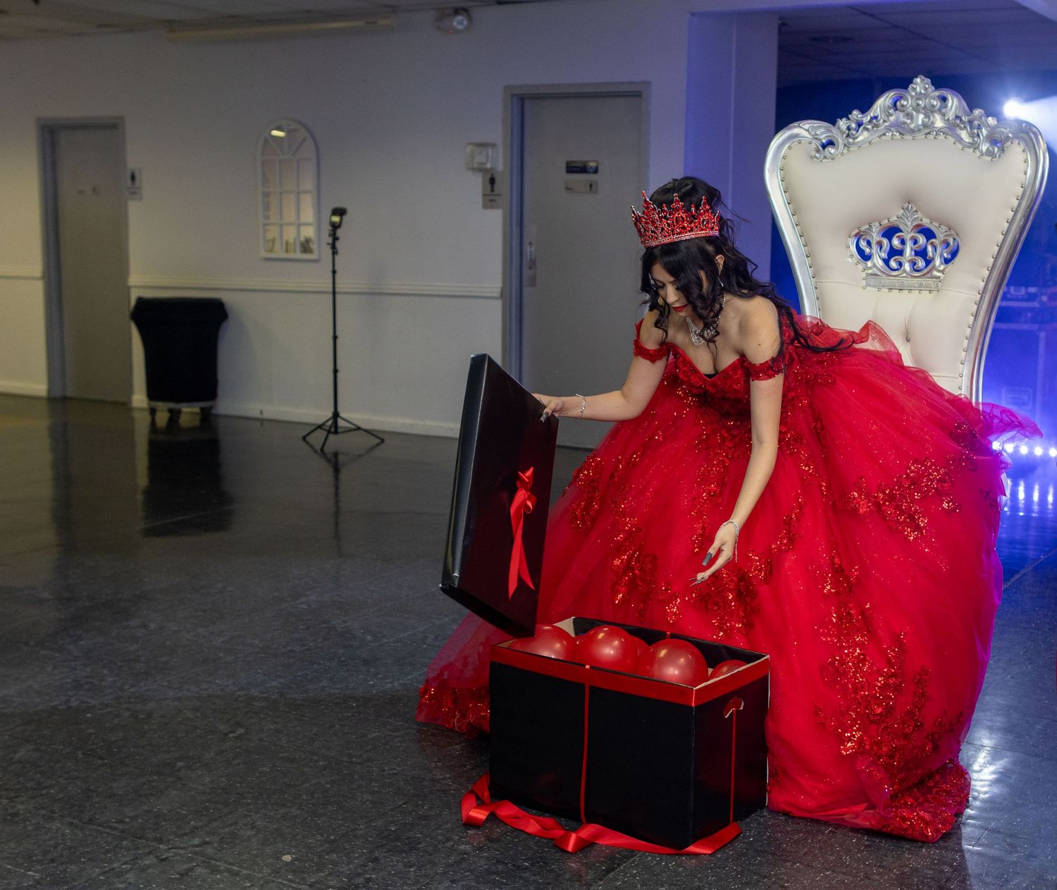 A stunning red ball gown with crystal embellishments is displayed in dramatic lighting against a dark background.