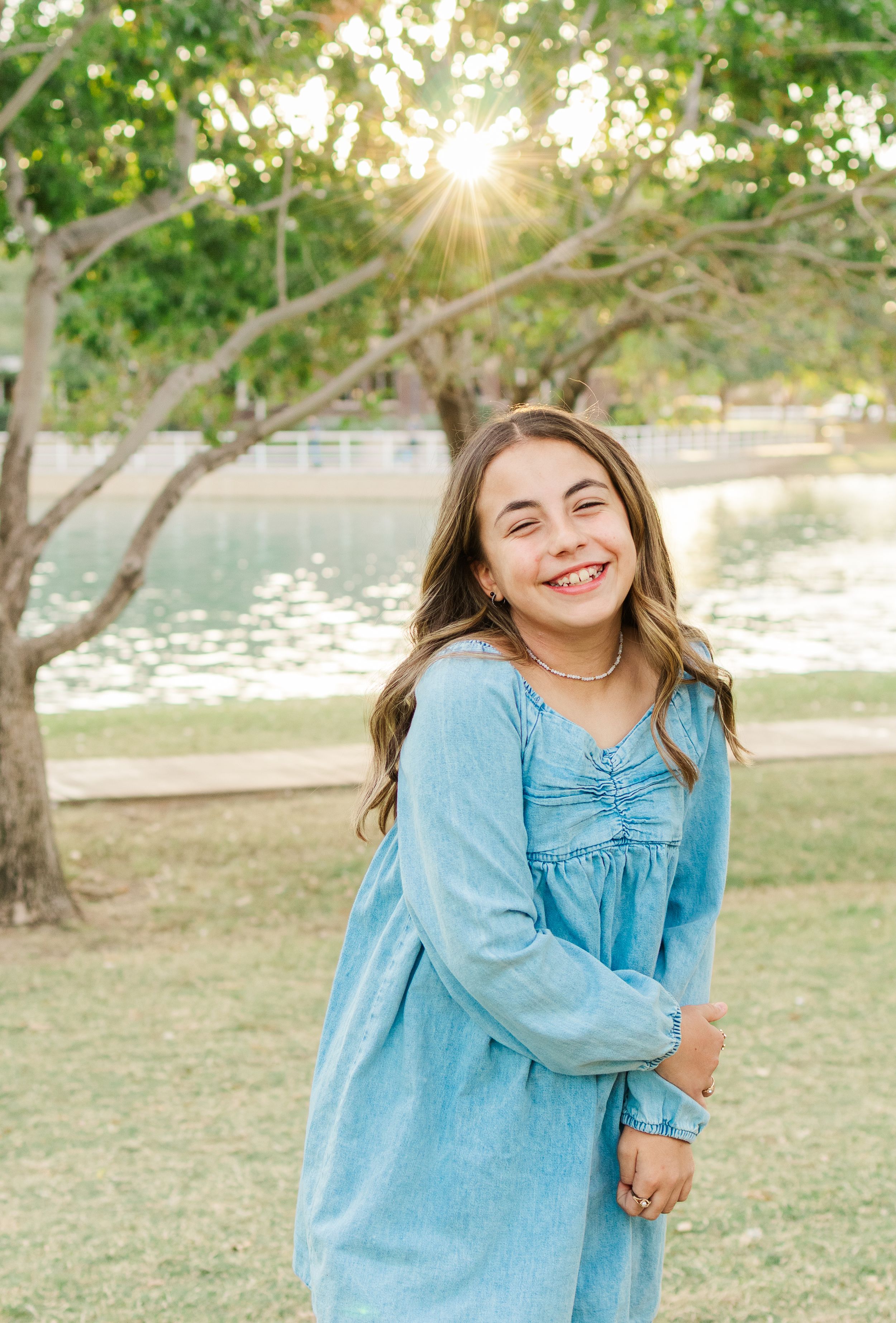 Light and airy portrait of a young girl smiling underneath a tree at golden hour in Morrison Ranch in Gilbert, Arizona.
