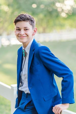 Light and airy portrait of a young teenage boy in a blue suit smiling at Morrison Ranch park in Gilbert, Arizona.