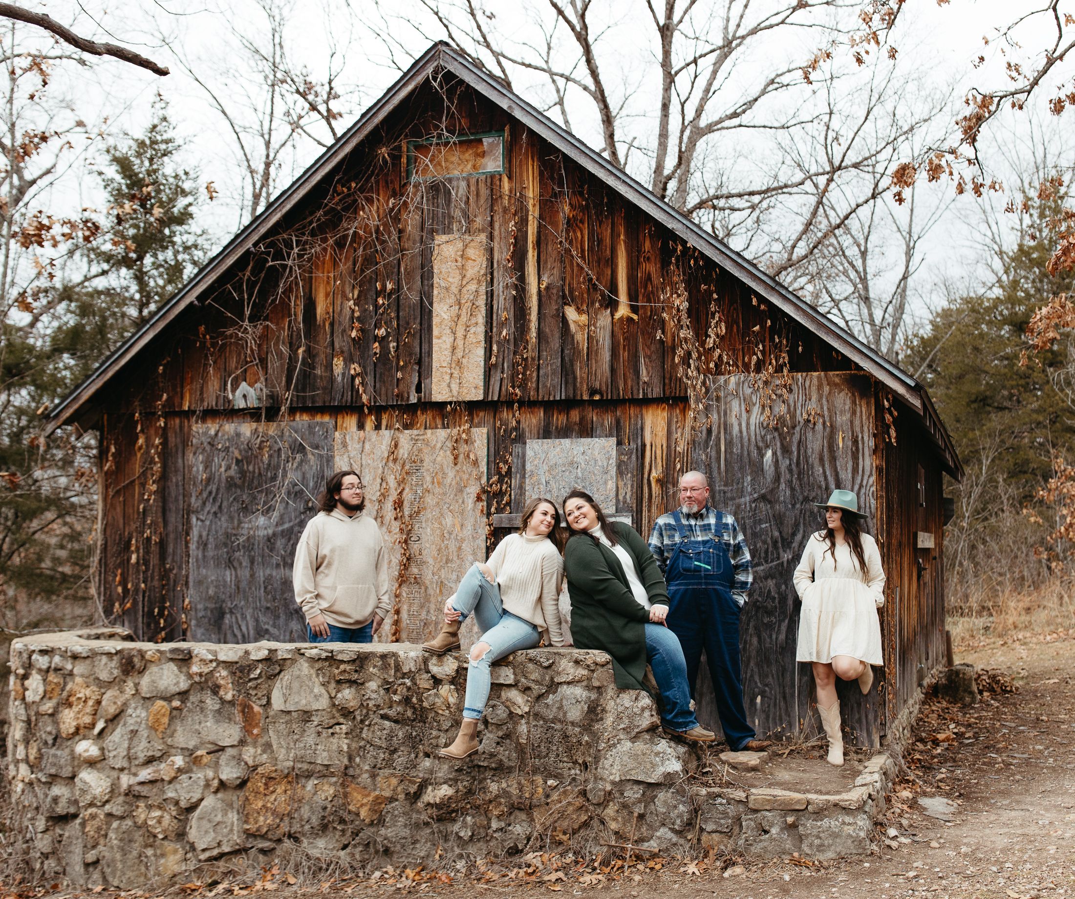 A weathered wooden barn with rustic stone wall foundation surrounded by autumn trees.