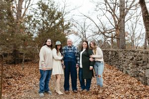 A group of people standing together on fallen autumn leaves next to a stone wall in a wooded area.