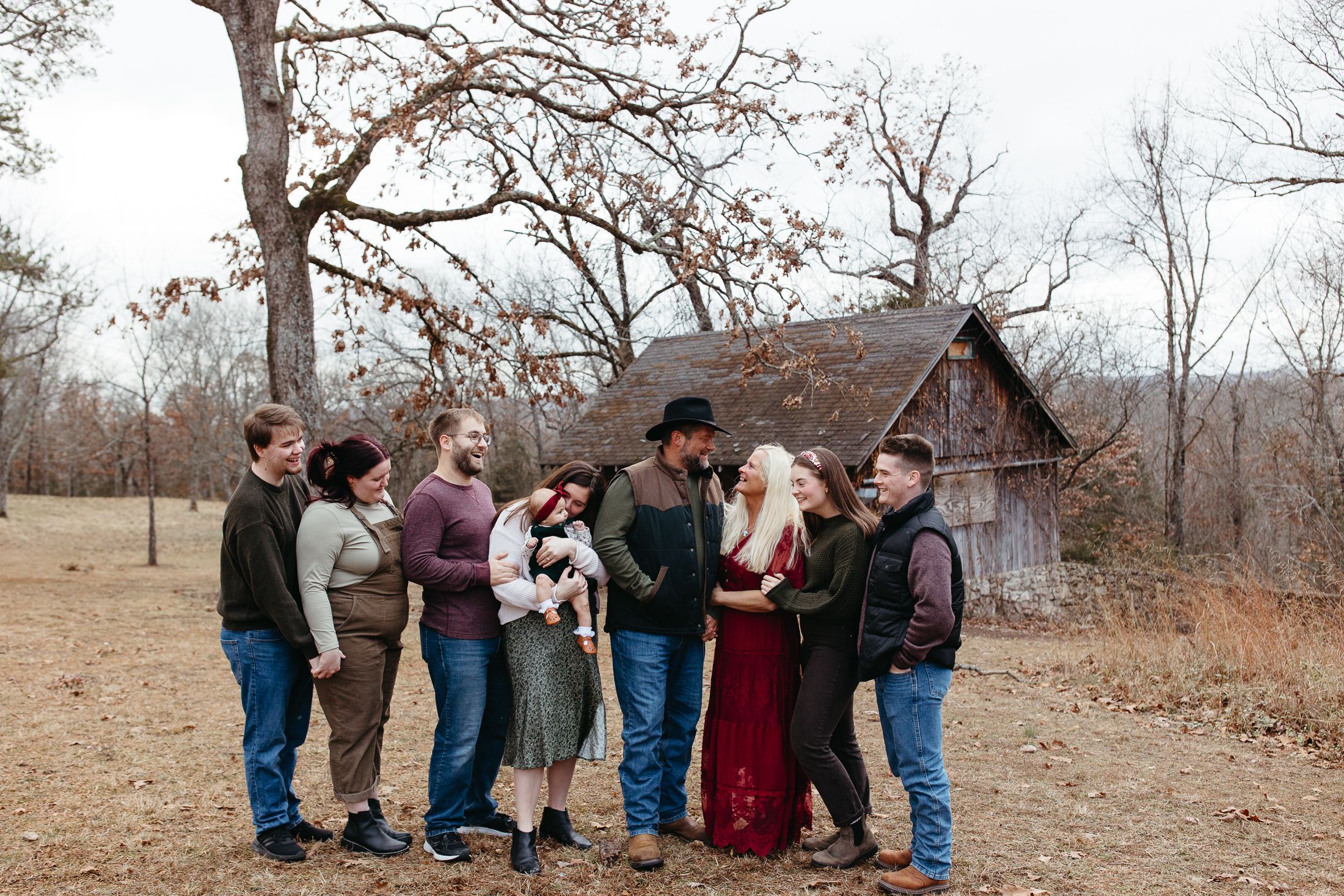 A group stands together in front of a rustic cabin on a winter day with bare trees in the background.