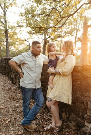 A couple dances playfully among fallen leaves in a sunlit forest during a romantic autumn photoshoot.