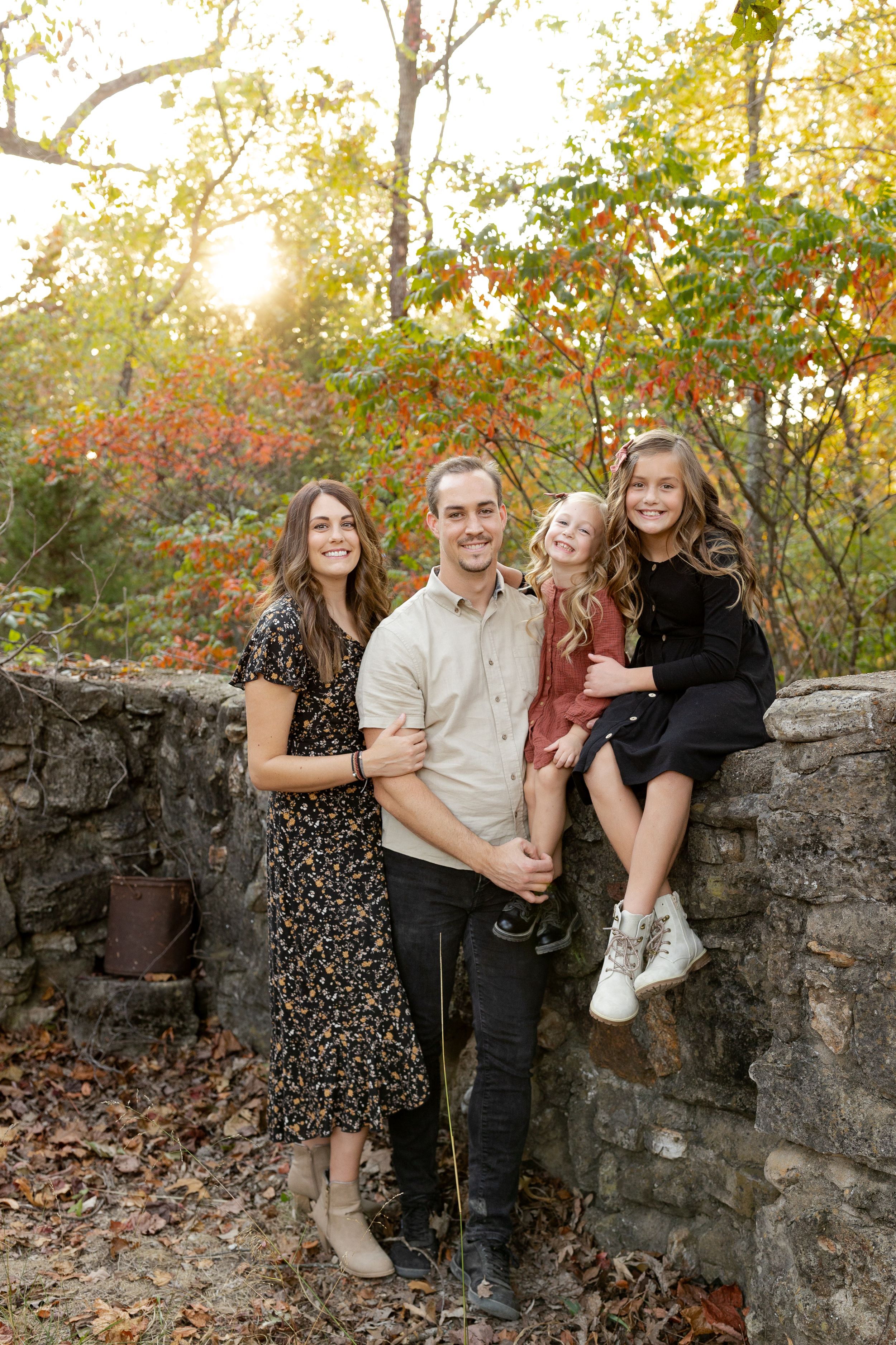 A group stands together by a stone wall during autumn with sunlight filtering through colorful fall foliage.