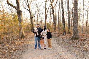 A group of people walk along a wooded trail surrounded by bare autumn trees and fallen leaves.
