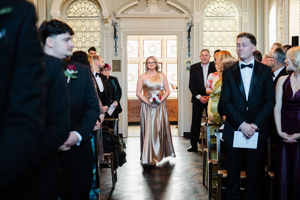 Elegant wedding party dances and celebrates in a grand ballroom with ornate white walls and large windows.