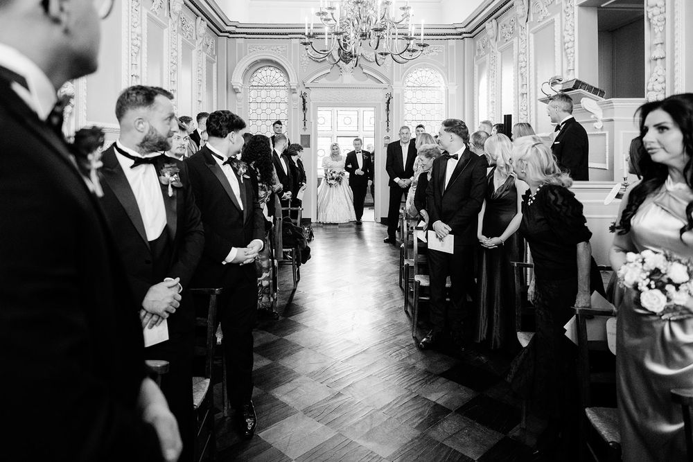 Elegant wedding reception guests mingle in a grand ballroom with ornate chandeliers and classic decor.