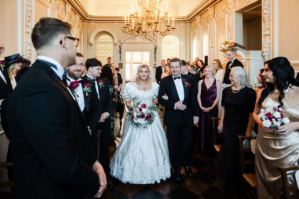 Wedding guests dance and celebrate during an elegant reception in an ornate ballroom with crystal chandeliers.
