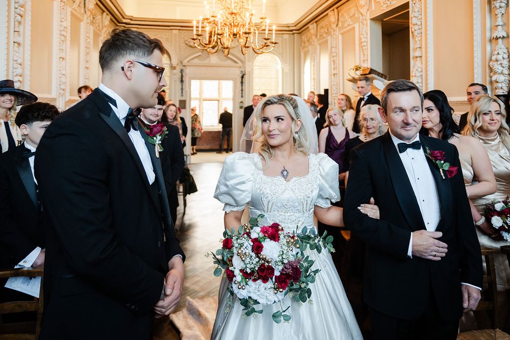 Wedding party celebrates in an elegant ballroom with ornate chandeliers and classic decor during a formal reception.