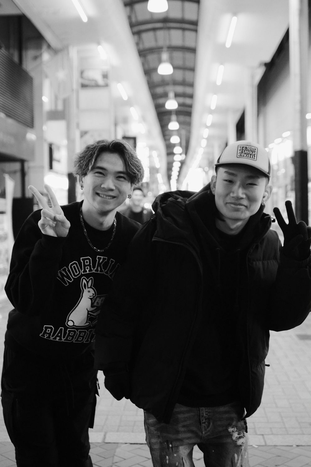 A group of people in black hoodies and casual wear pose together in a bright indoor hallway.