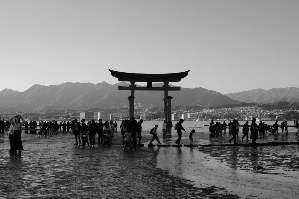 Silhouetted crowds gather around the iconic Torii gate at Miyajima's Itsukushima Shrine during high tide in Japan.