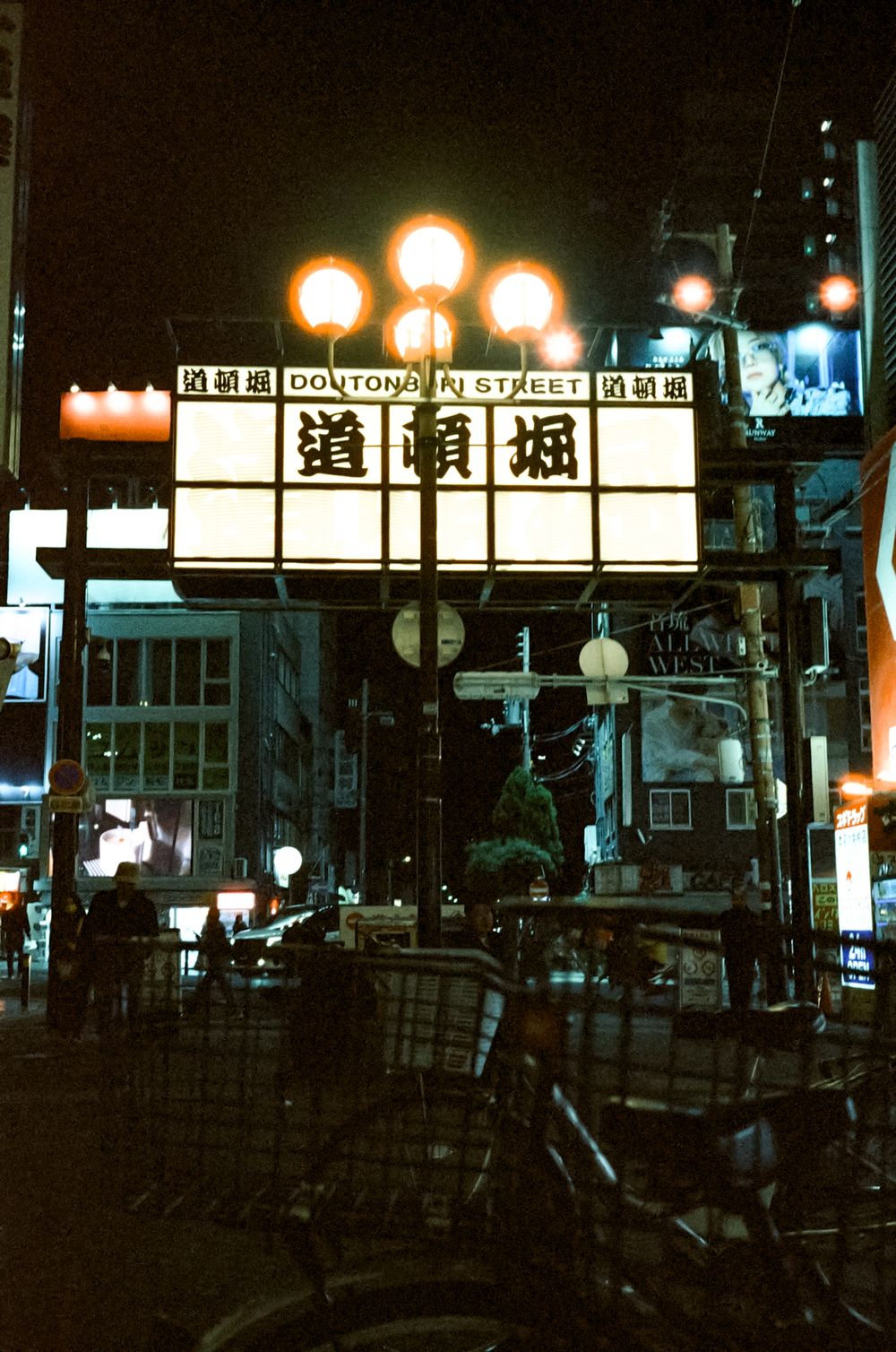 Illuminated Japanese street signs and lanterns glow against a dark urban nightscape.