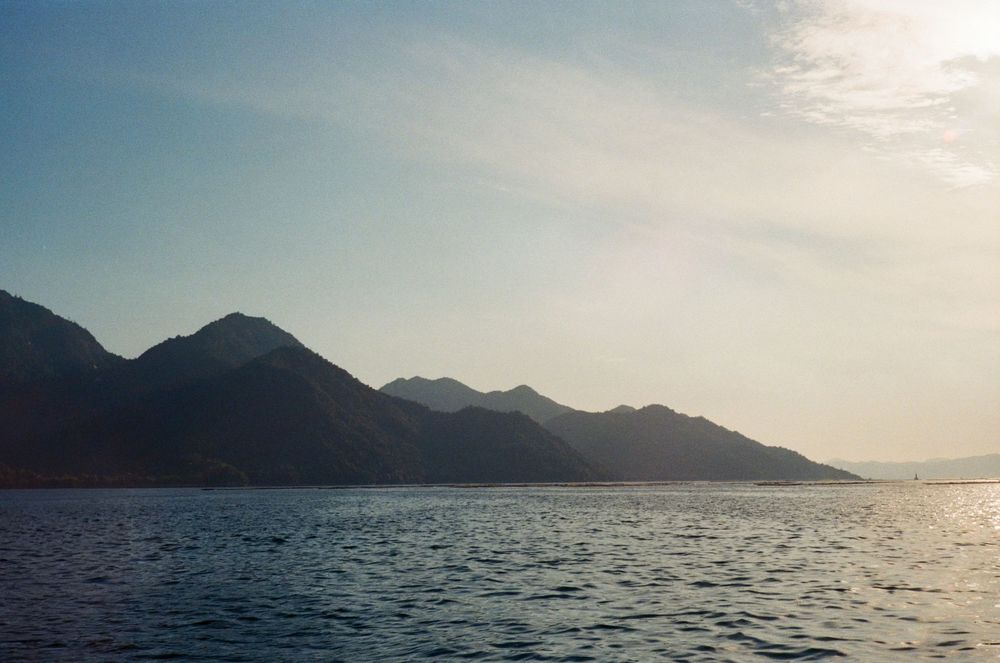 Panoramic view of a serene mountain lake with calm waters reflecting the sunlight during golden hour.