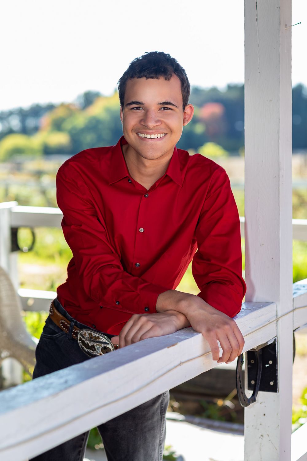 Portrait session on a white porch railing with bright red shirt against natural outdoor backdrop.