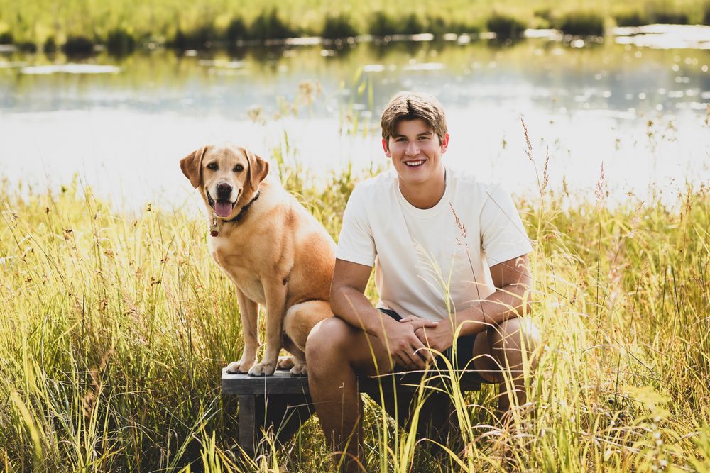 Golden retriever and companion sitting by lake during sunset in natural setting.