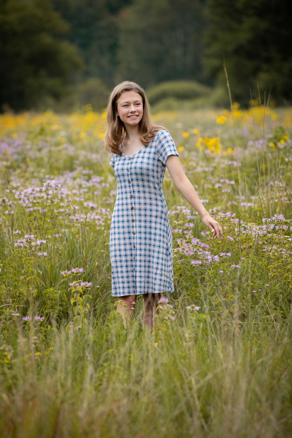 Person in checkered dress twirling through wildflower field during summer.