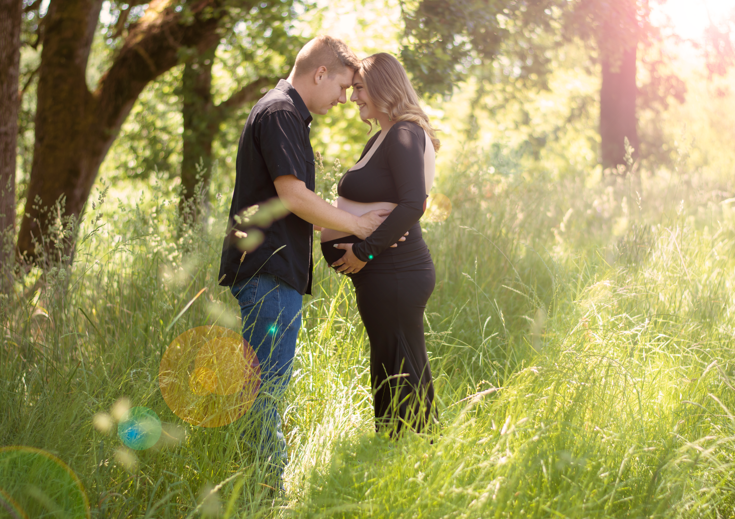 Sun-dappled maternity photography session in tall grass with golden hour lighting.