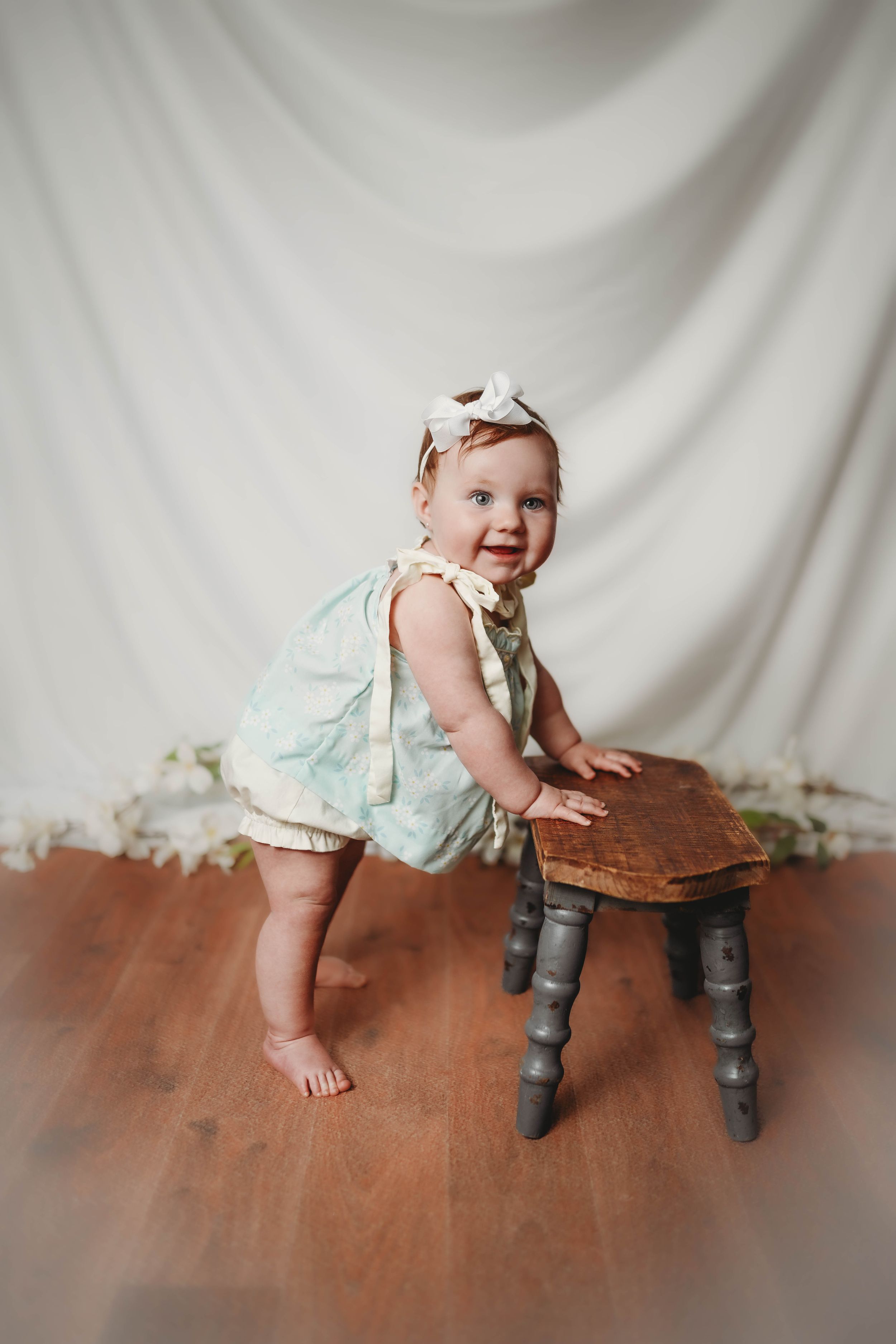 Baby in mint dress crawling and playing on wooden floor against white backdrop.