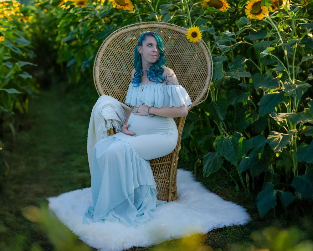 Ethereal white dress contrasts with vibrant sunflowers in garden scene featuring wicker peacock chair and soft white rug.